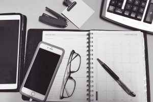black and white photo of flat lay desk with calculator pen spectacles and iphone