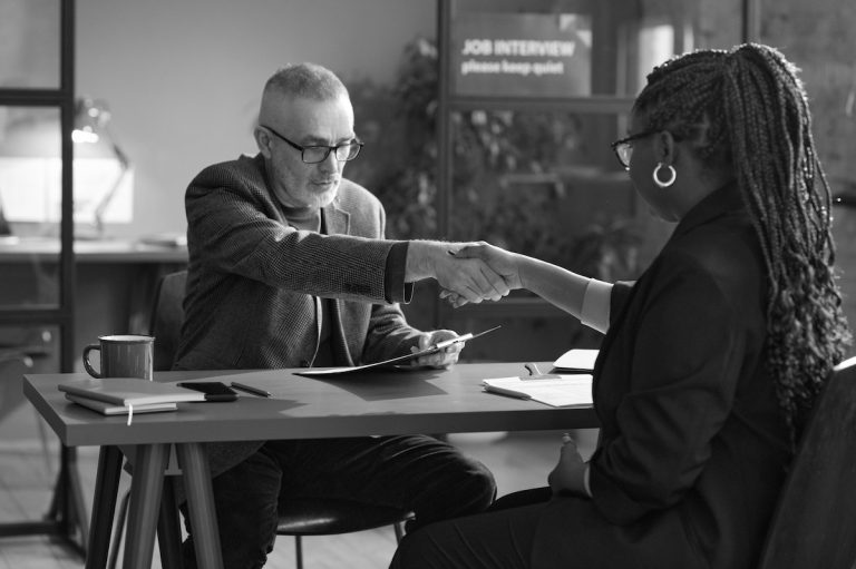 manager shaking hands with young woman while they sitting at table during job interview